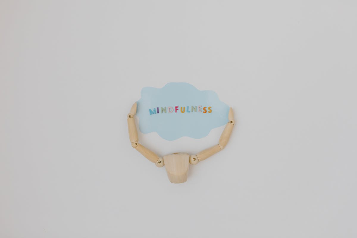 Een houten figuurtje houdt een tekstballon vast met het woord 'Mindfulness'
